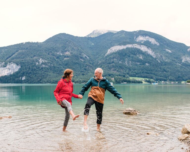 Ein älteres Ehepaar spritzt glücklich mit den Füssen Wasser aus einem See