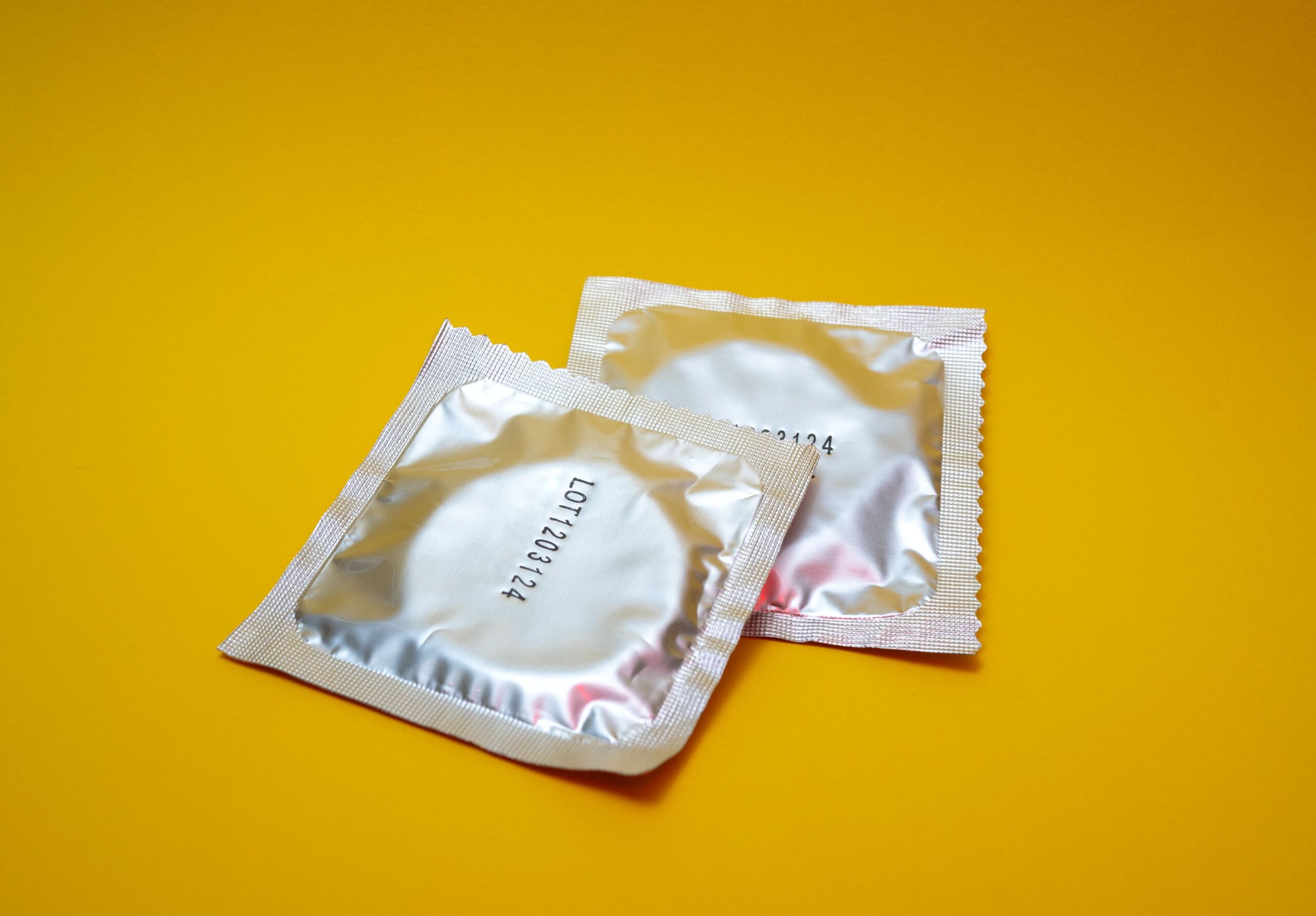 Two wrapped condoms on a yellow background