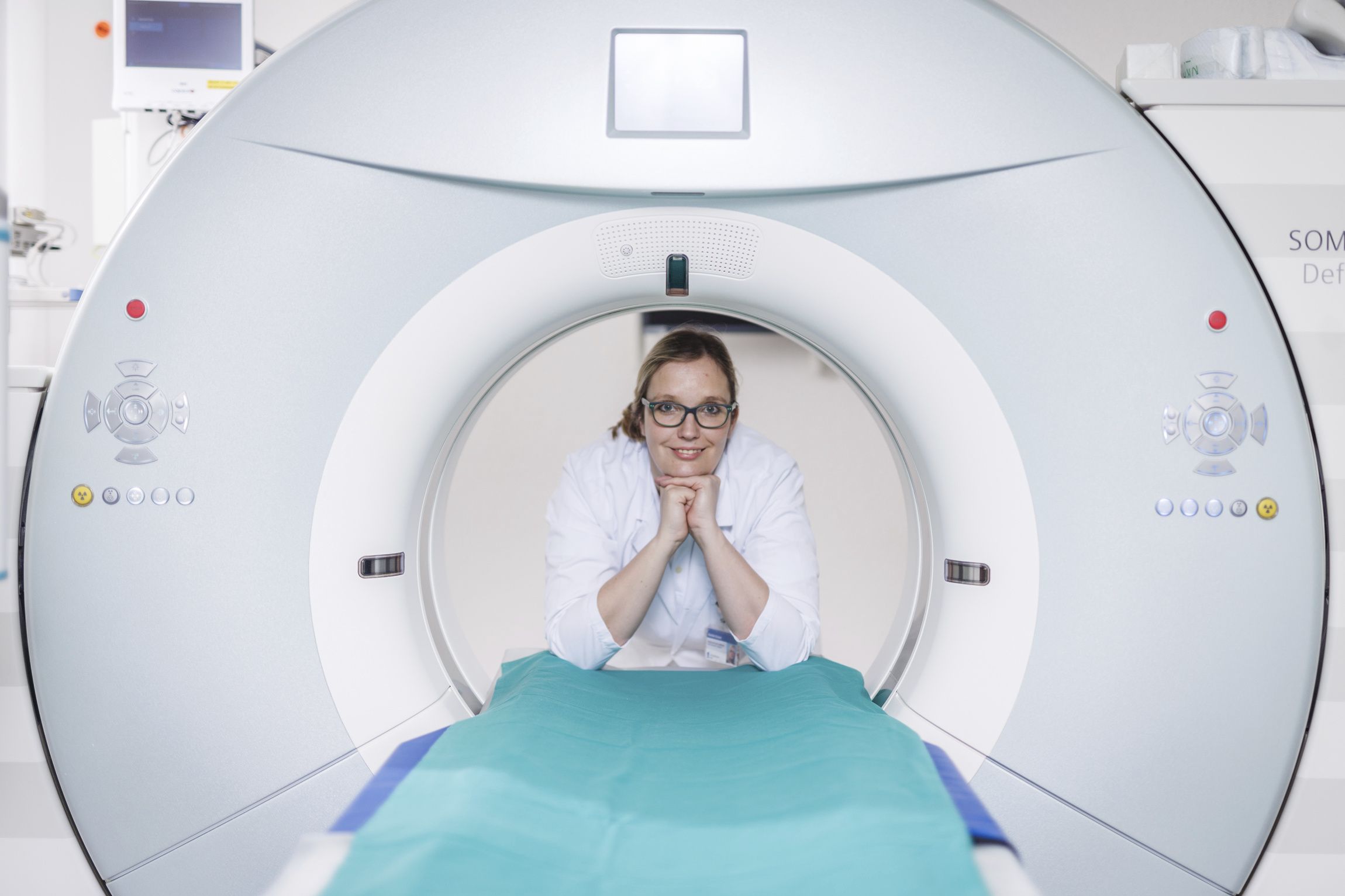 A female doctor stands smiling behind an MRI machine