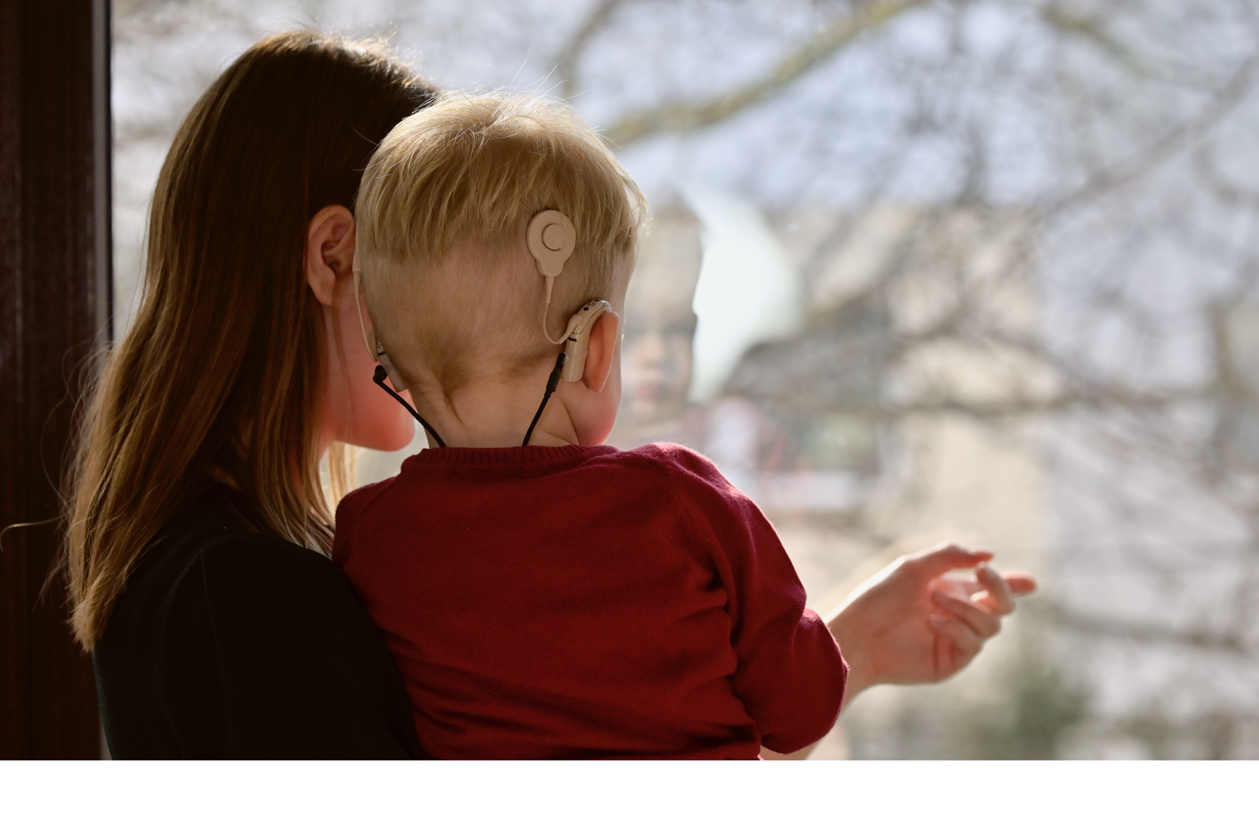 Mutter hält Kind mit einem implantierten Cochlea Implantat in der Hand.
