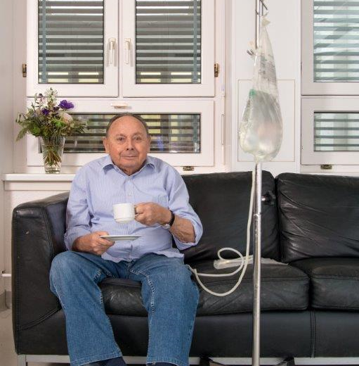 Ein Dialysepatient sitzt während seiner Behandlung auf einem Sofa und trinkt einen Kaffee