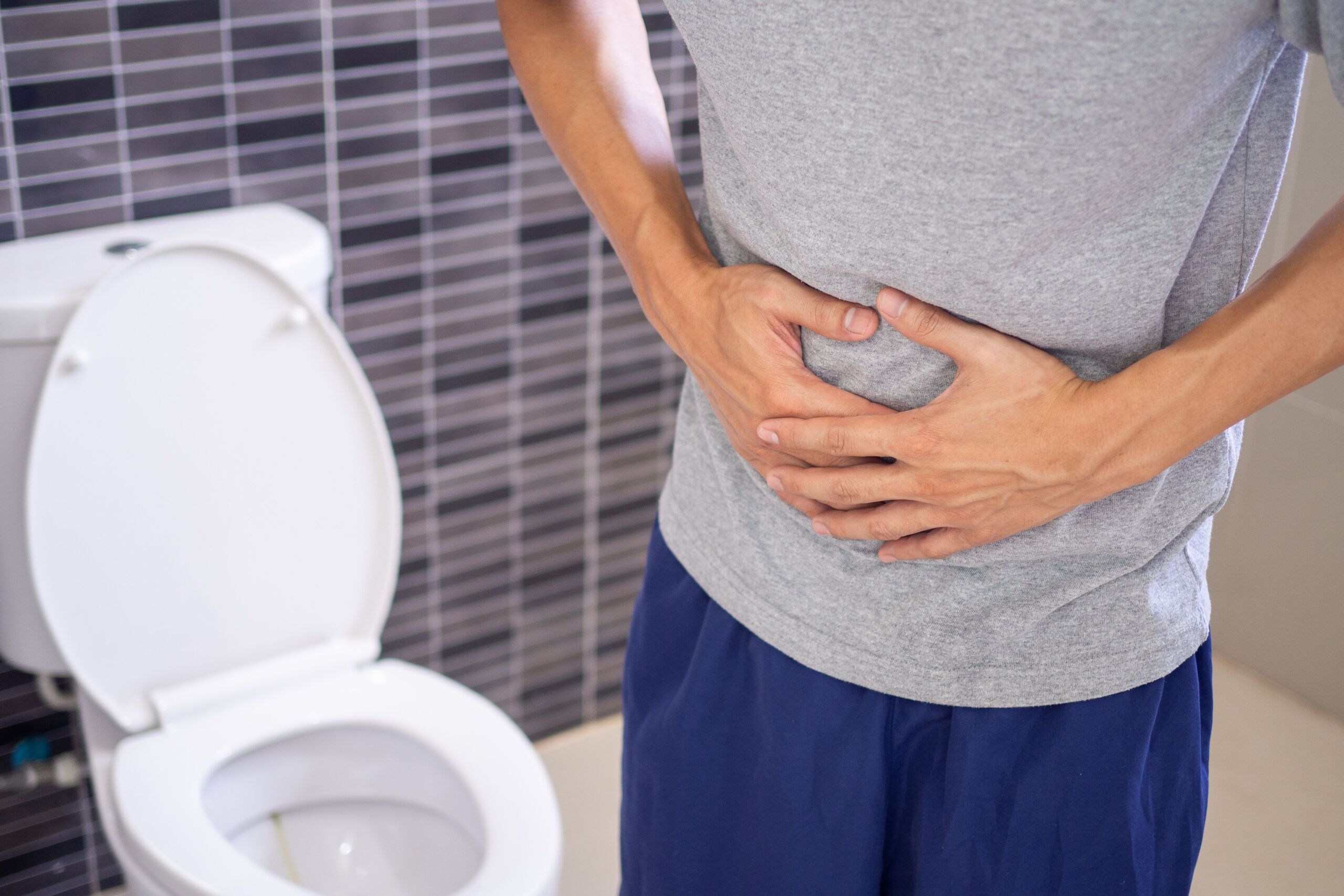 Mann steht vor einer Toilette und hält die Hände an den Bauch