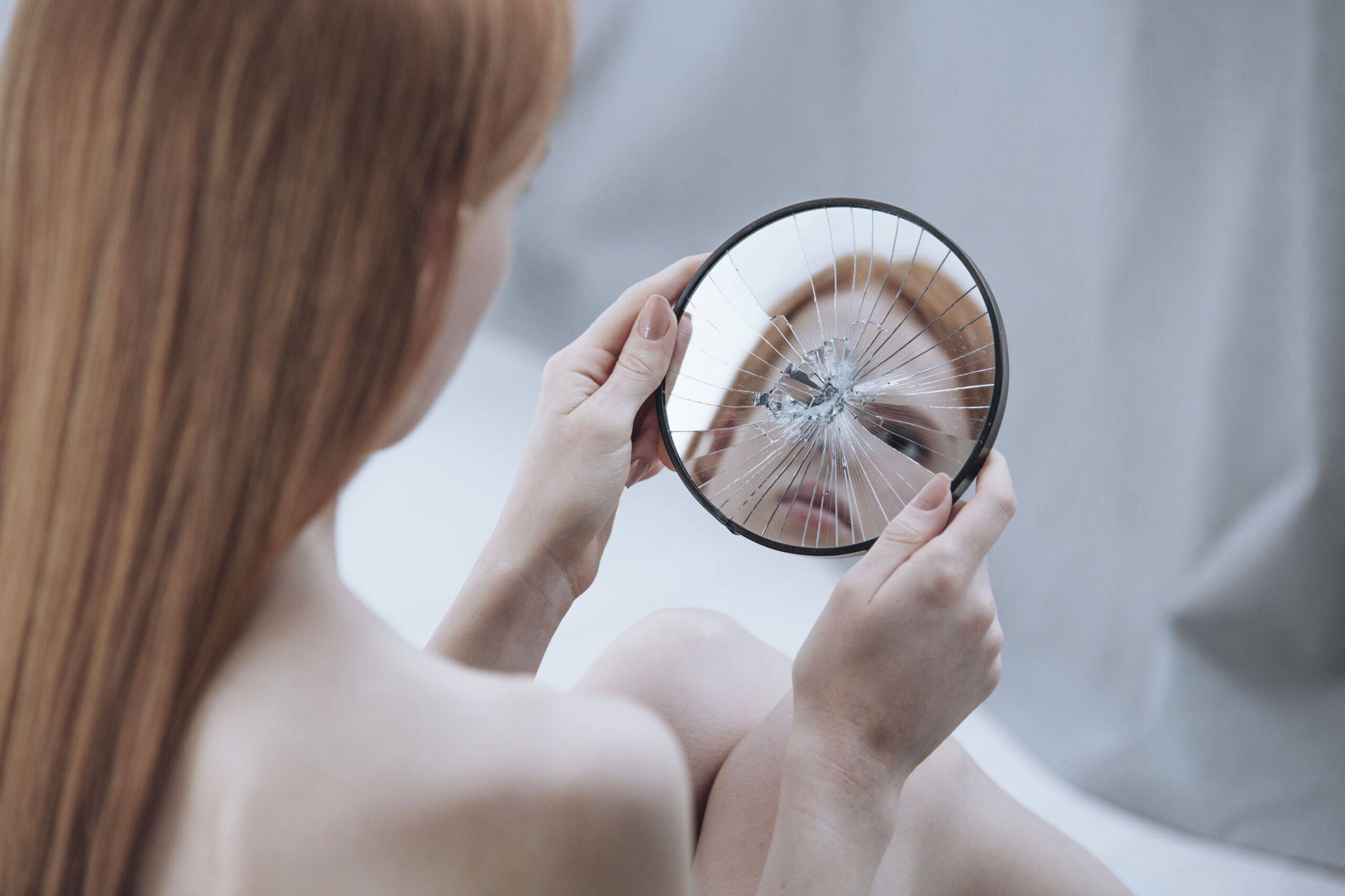 Frau sieht sich in einem zerbrochenen Spiegel an