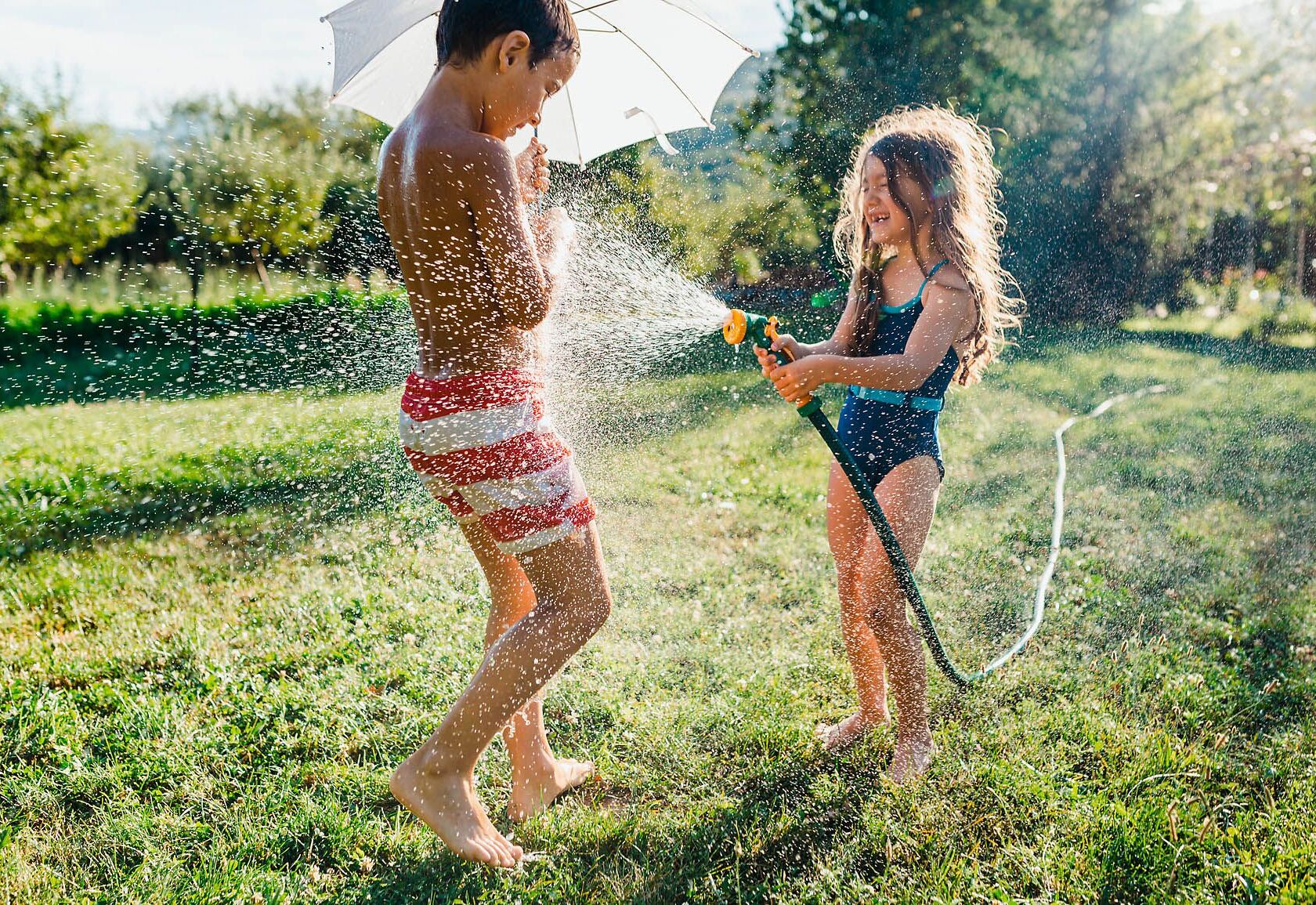 zwei Kinder die im Garten mit einem Wasserschlauch spielen