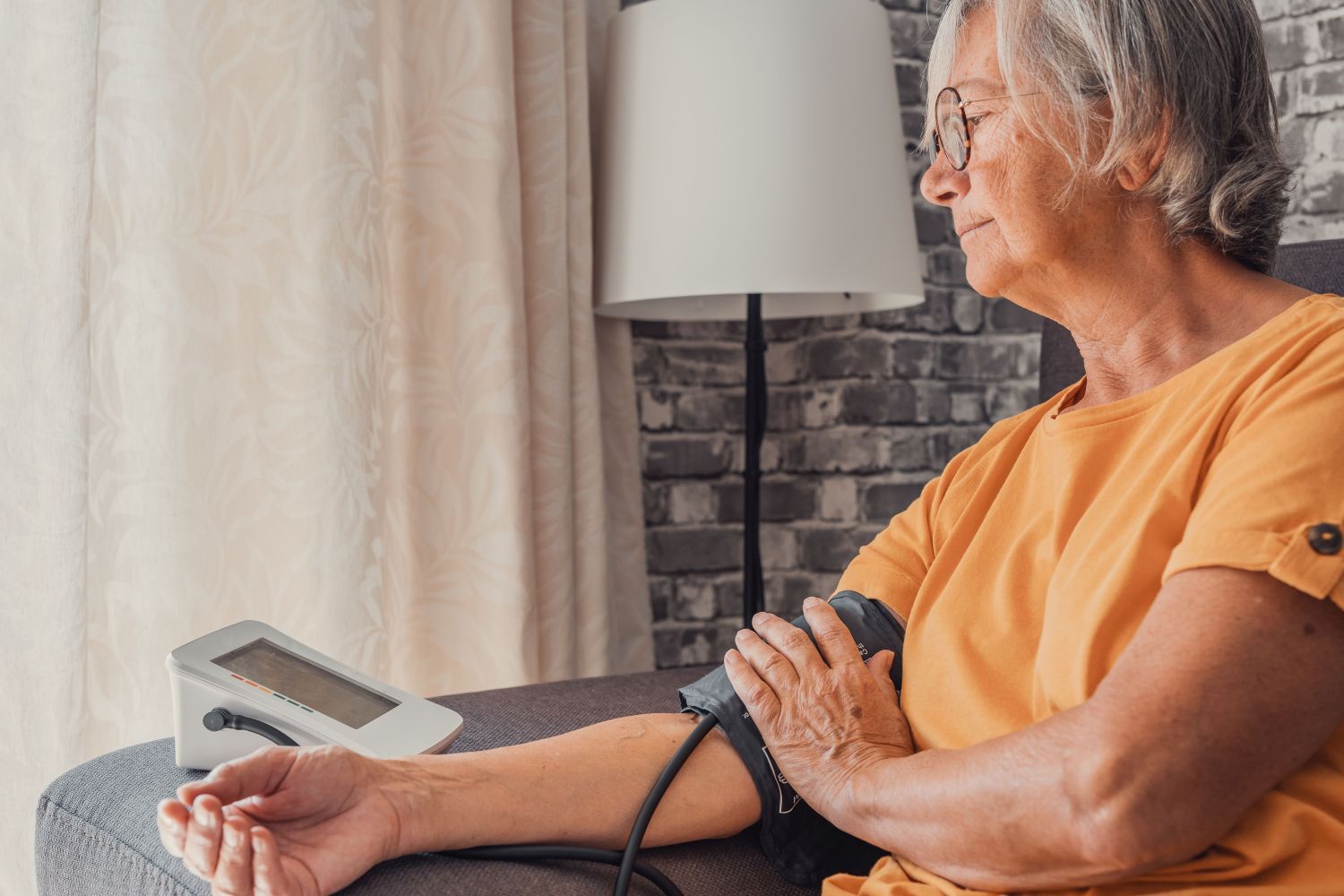 Ältere Dame misst sitzend ihren Blutdruck mit Messgerät