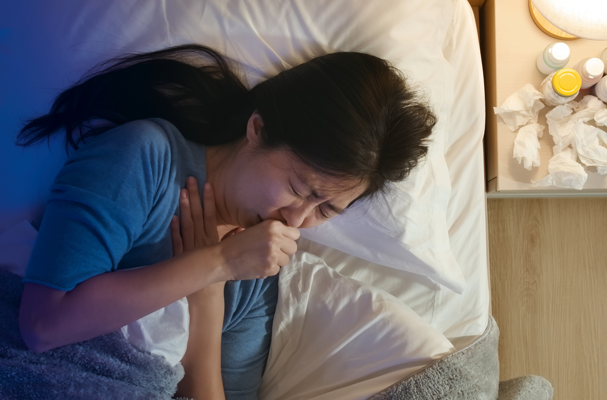 Frau liegt im Bett und hustet