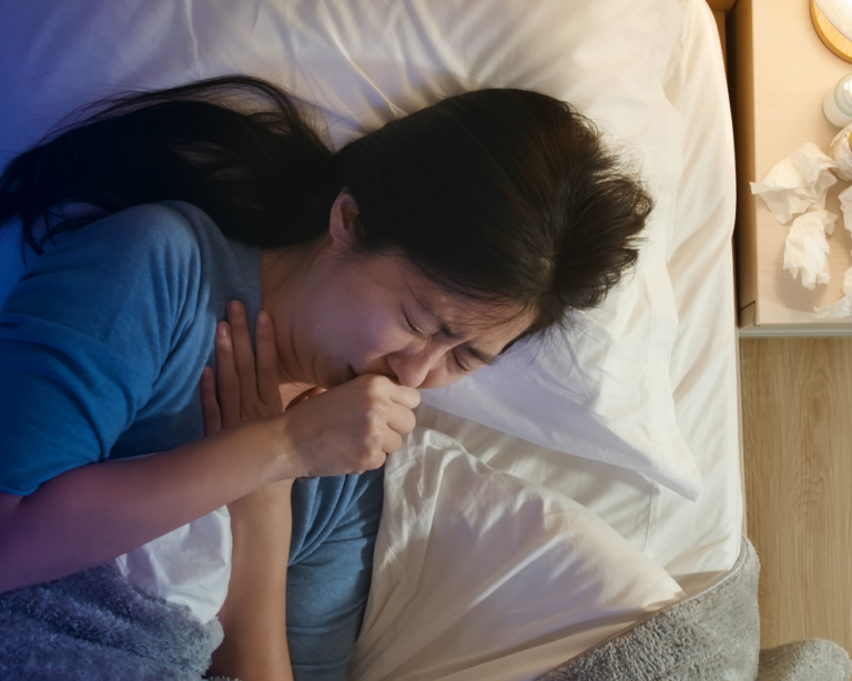 Frau liegt im Bett und hustet