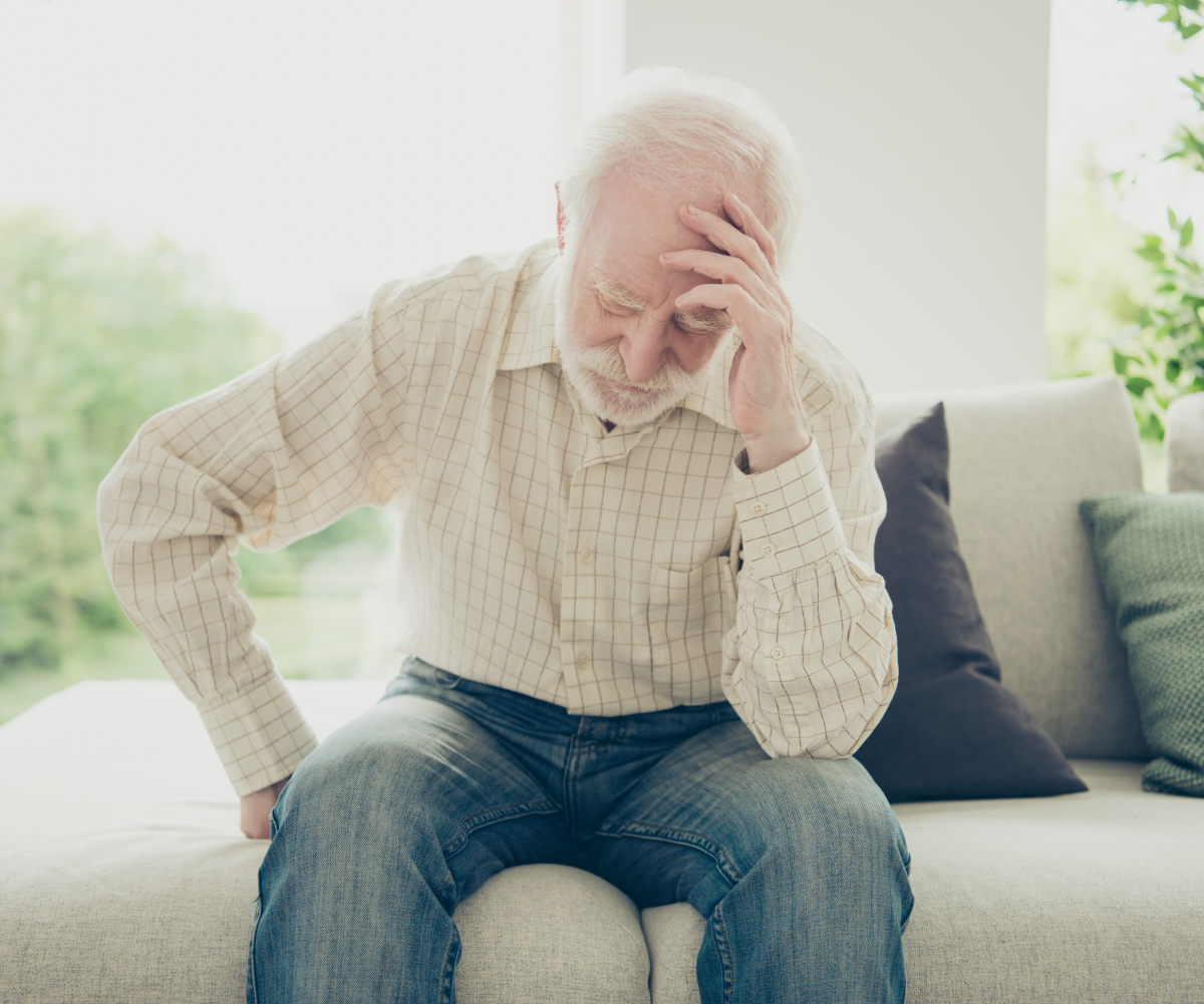 Alter Mann sitzt auf Sofa und hält sich den Kopf