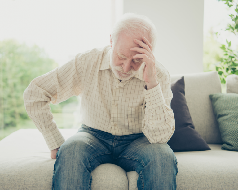 Alter Mann sitzt auf Sofa und hält sich den Kopf