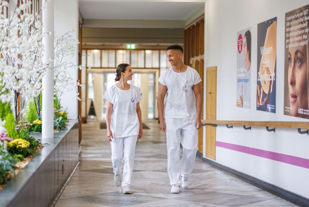 Zwei Pflegefachpersonen laufen nebeneinander und lachen sich an.