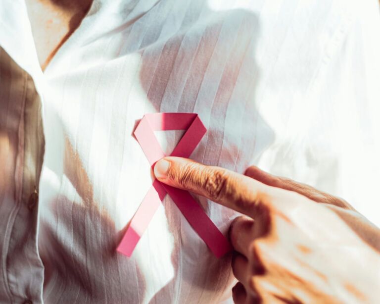 Frau hält sich rote Schleife an Brust