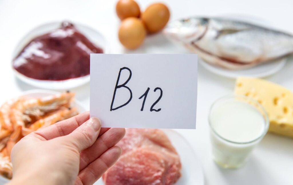 Hand mit Zettel B12, im Hintergrund Lebensmittel