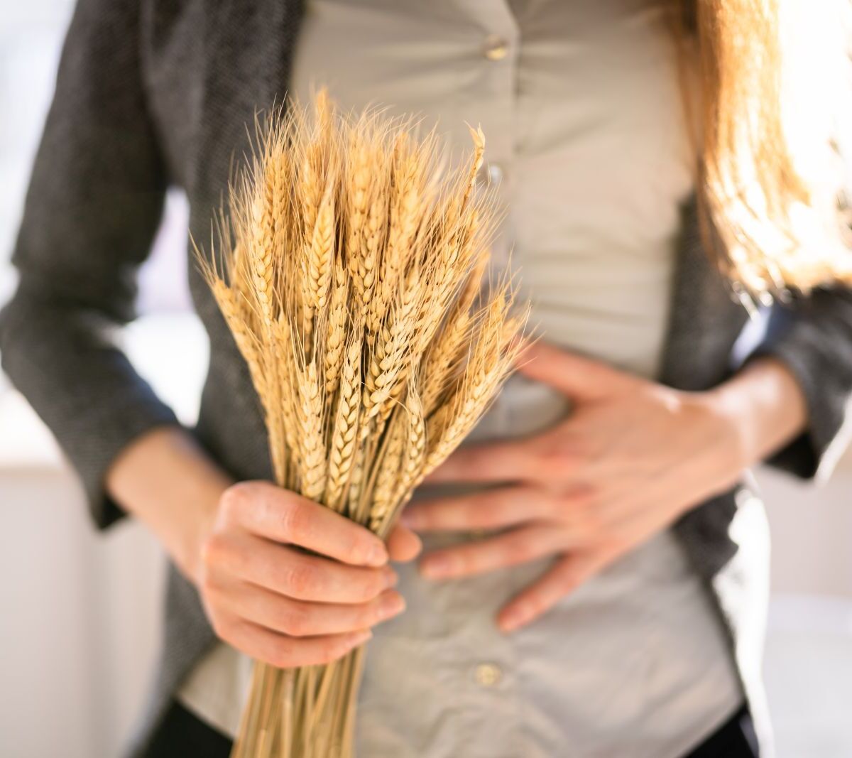 Bild von einer Frau, die Bauchschmerzen hat und Weizen in der Hand hält
