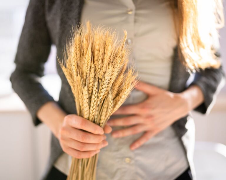 Bild von einer Frau, die Bauchschmerzen hat und Weizen in der Hand hält