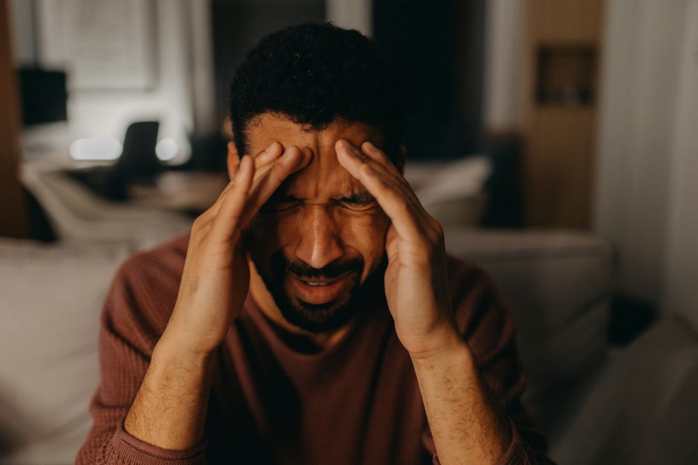 Mann hält sich Hände an Stirn, schmerzverzerrtes Gesicht