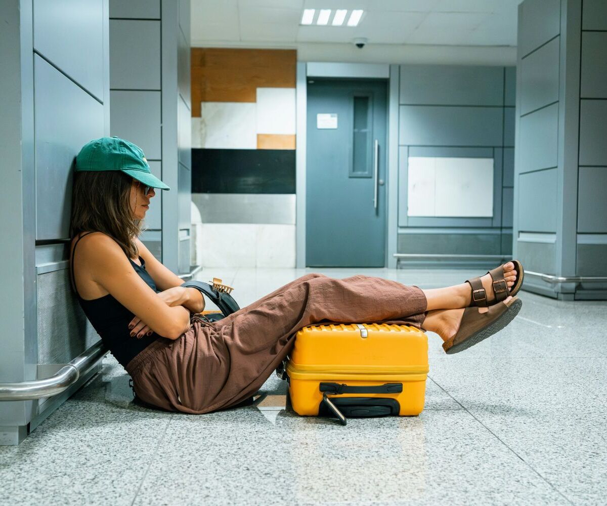 Frau sitzt am Flughafen mit Koffer unter den Beinen und döst